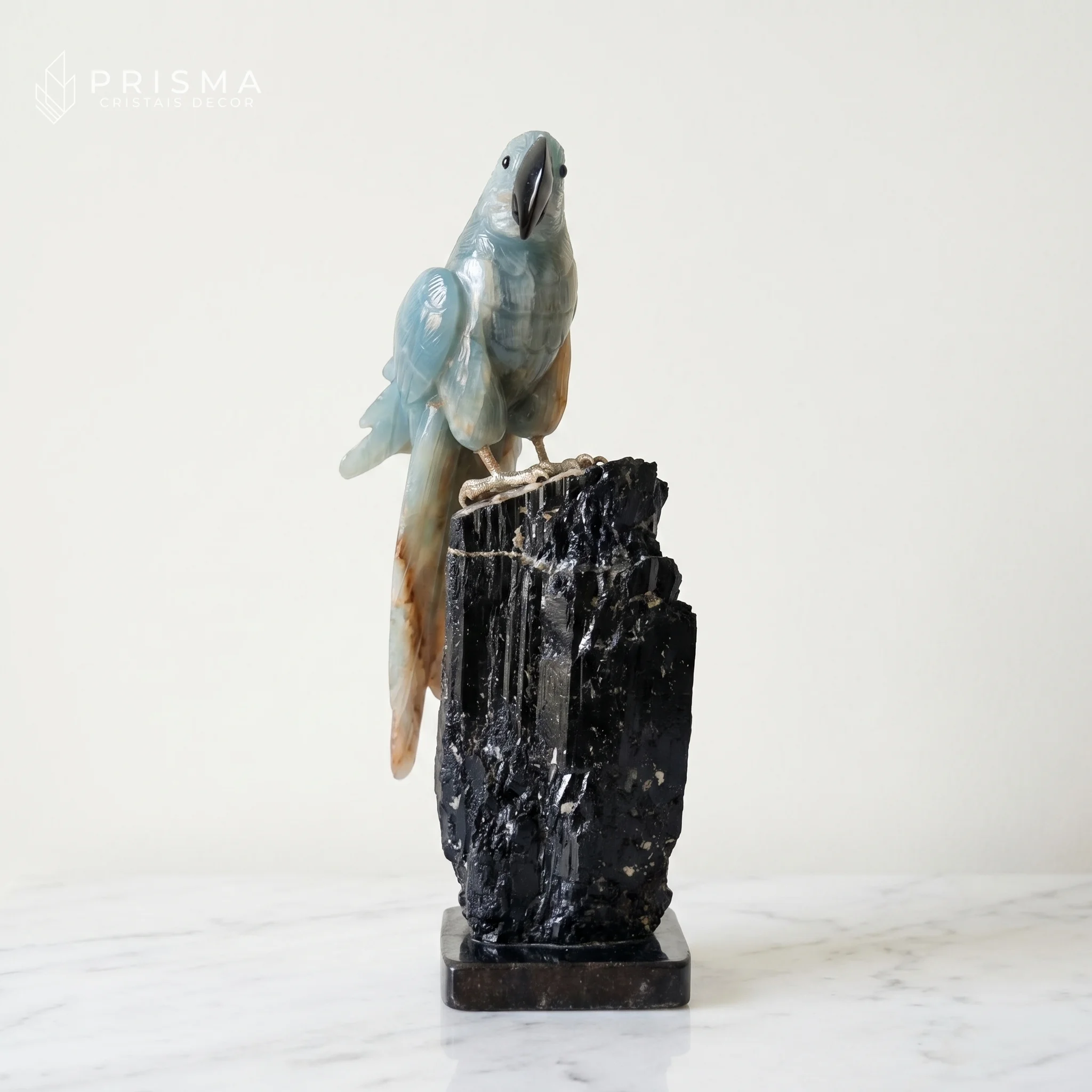 Arara Ônix Azul em composição minimalista sobre mármore branco — base de turmalina negra, luz natural difusa, decoração premium Savassi BH