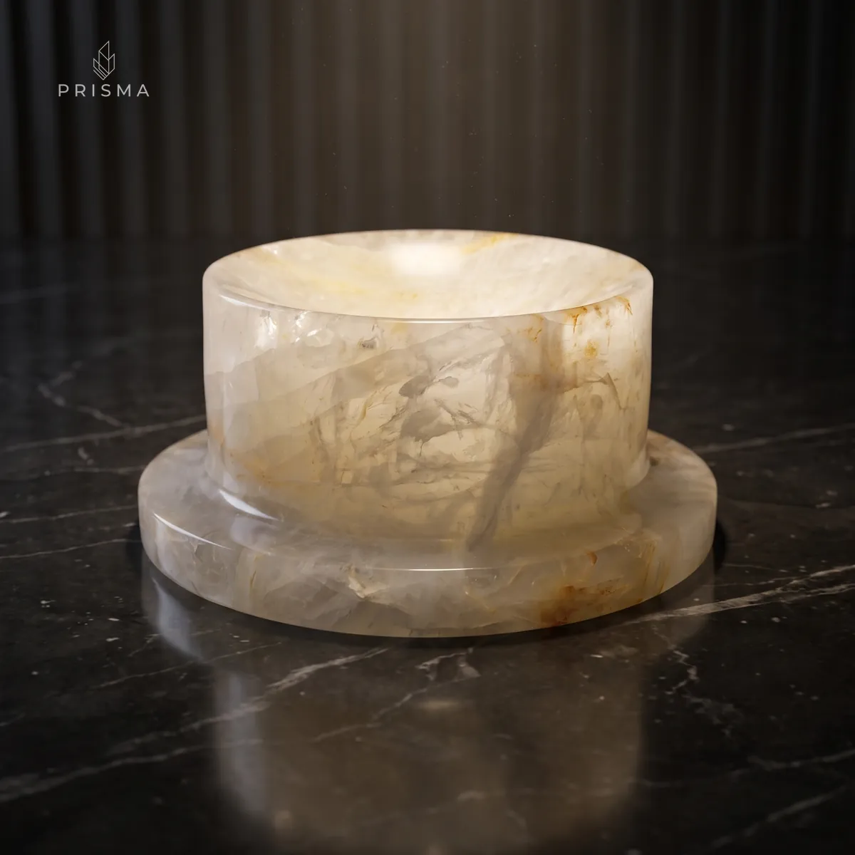Comedouro de pedra em quartzo hematoide com veios dourados sobre piso de mármore escuro, iluminado por foco de luz